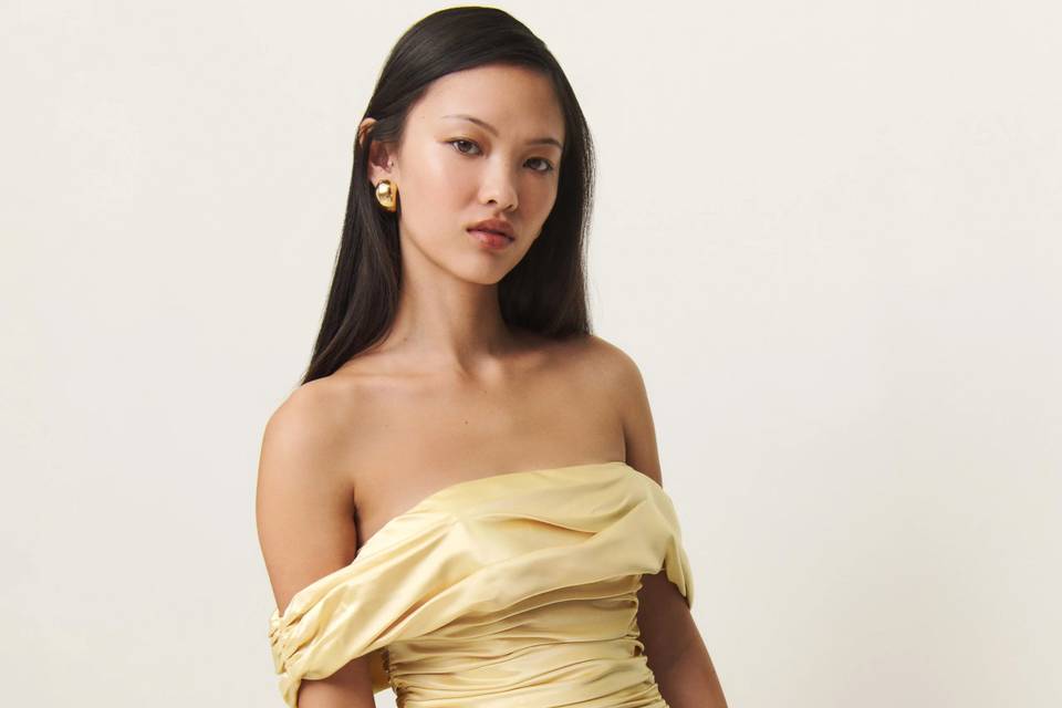 Model with long dark straight hair wearing an off-shoulder yellow bridesmaid dress with ruched bodice