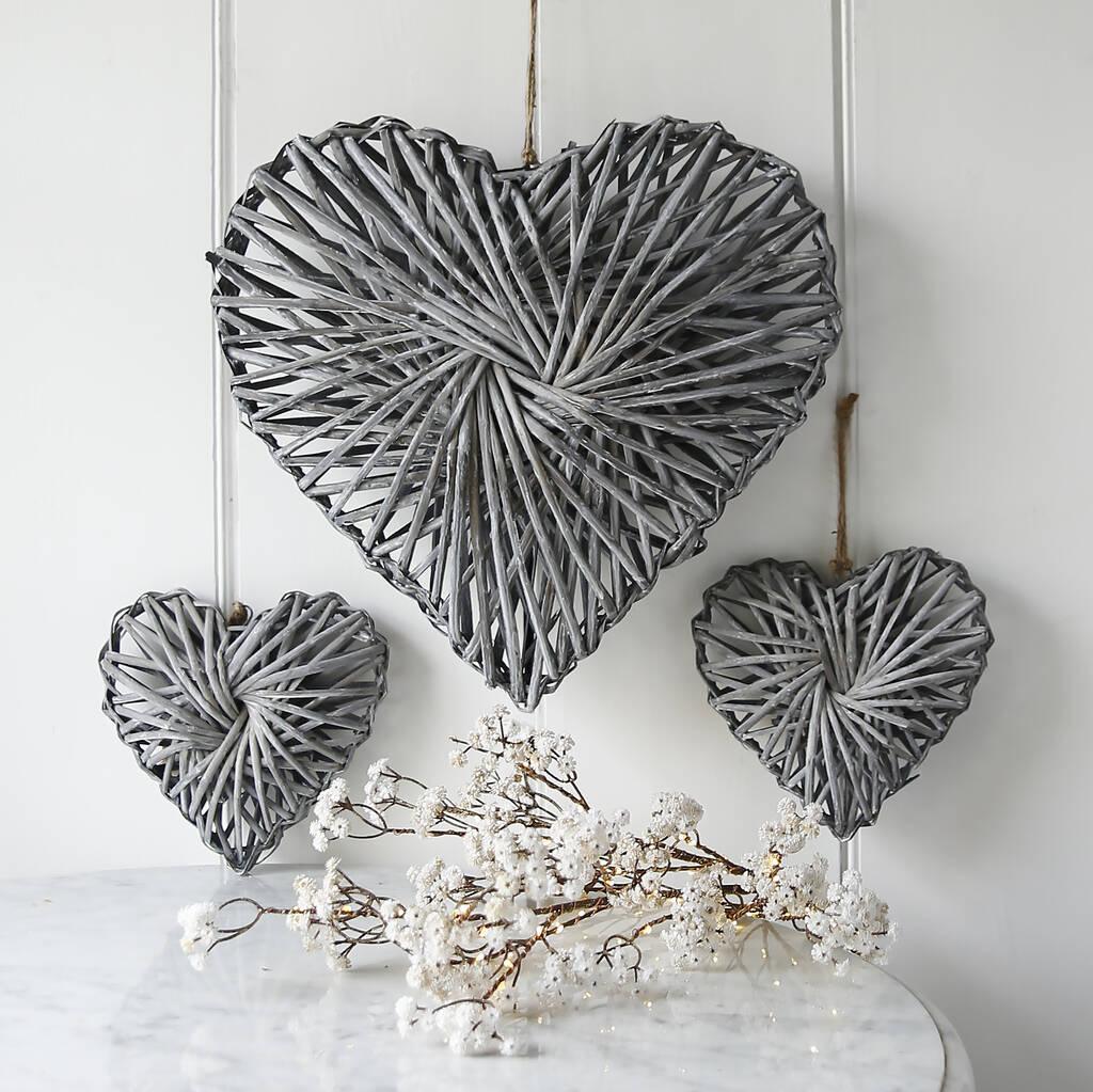Three grey-wash willow heart decorations hanging on a while wall. They're in varying sizes.