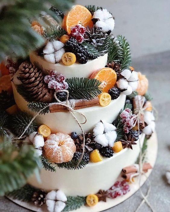 Three tiered rustic wedding cake with frosted berries, pinecones, fruit and cinnamon sticks