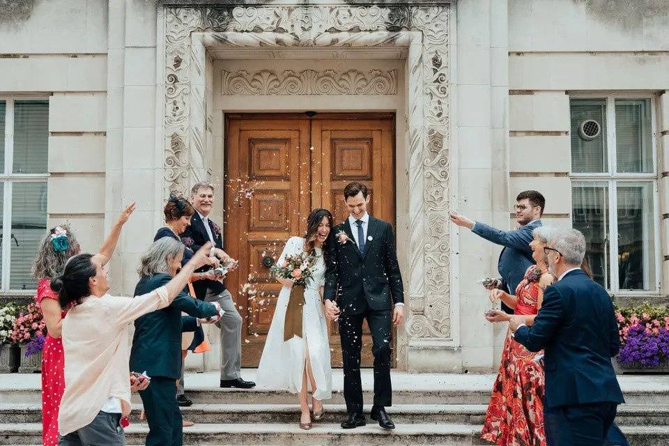 Bride and groom stand on the steps of wandsworth town hall while guests throw confetti