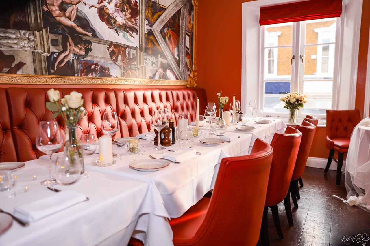 Interior of a restaurant with red seating, the table is set up for a wedding reception with flowers and glassware.