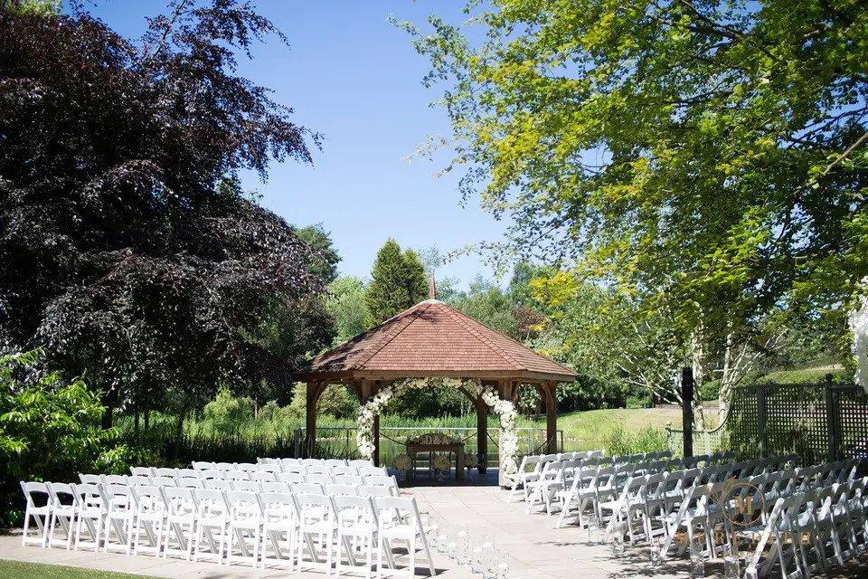 Outdoor wedding ceremony set up with pagoda, white folding chairs, floral arch and surrounding trees and forest