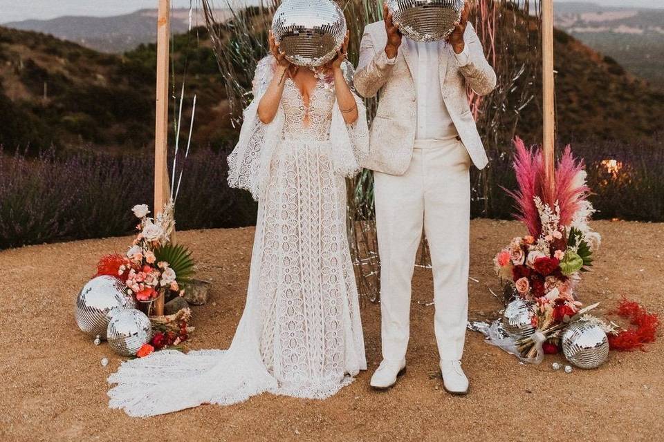 Couple standing by an arch outside holding disco balls