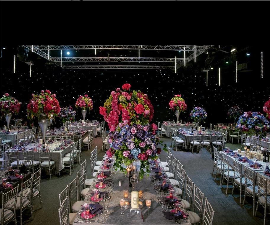 Interior of an events space set up for a large wedding with colourful floral displays on the long tables.