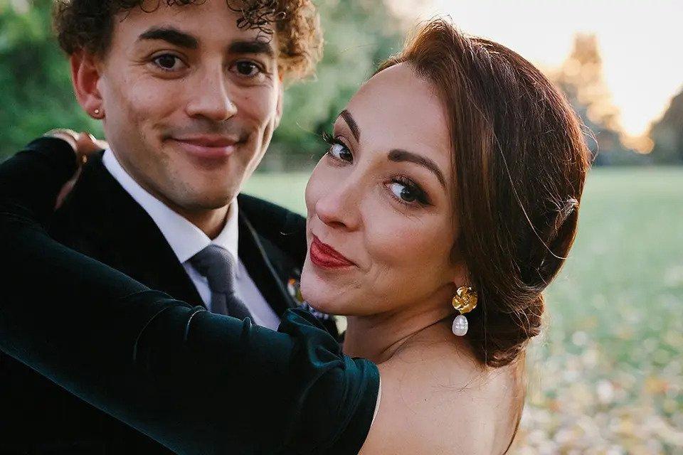 Bride and groom embrace outdoors while looking at the camera