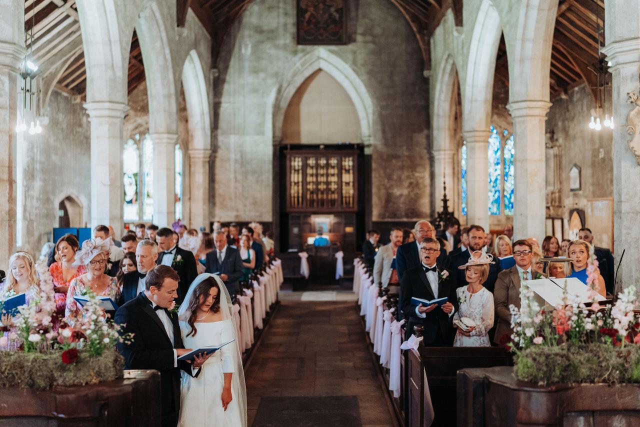 A bride and groom and their guests sing Christian hymns in a church ceremony.