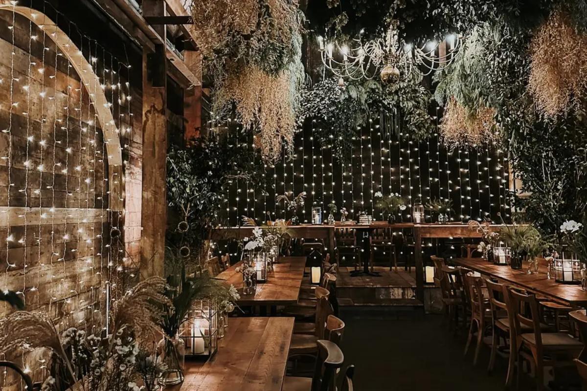 inside a rustic london wedding with fairy lights up the wall and wooden tables set up