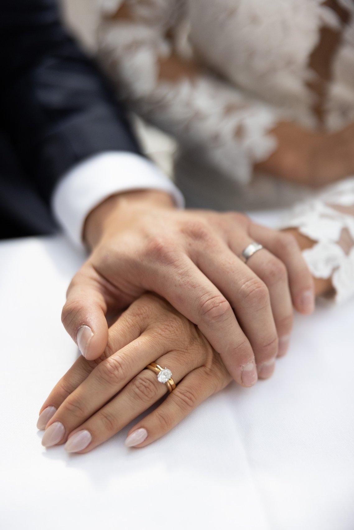 a close up of a bride's hand with an engagement ring and wedding band on and her groom's hand on top of hers