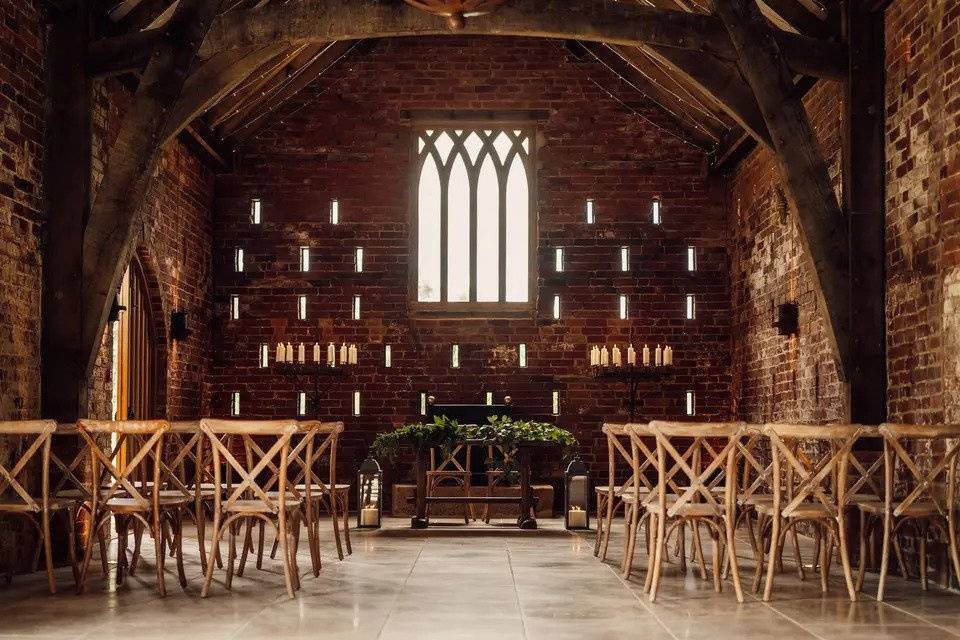 Ceremony room with exposed ref brick, a large window, candles, wooden chairs and a table with two chairs at the front of the room