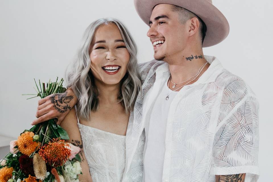A couple holding hands on their wedding day whilst holding a rustic bouquet and smiling