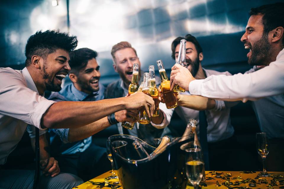 a group of guys playing stag do games in a bar and cheersing with beer bottles