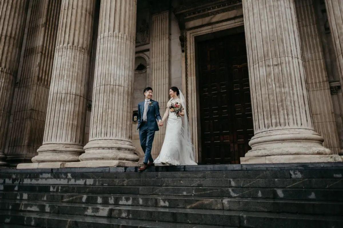a stylish couple hold hands and walk down the steps outside a town hall after getting married