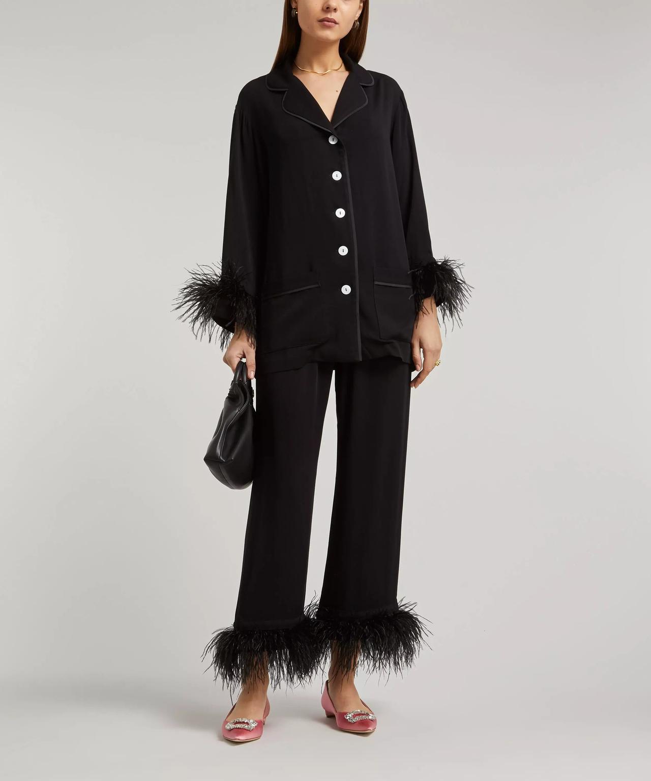 A model wearing a pair of silky black pyjamas trimmed at the wrists and ankles with black feathers