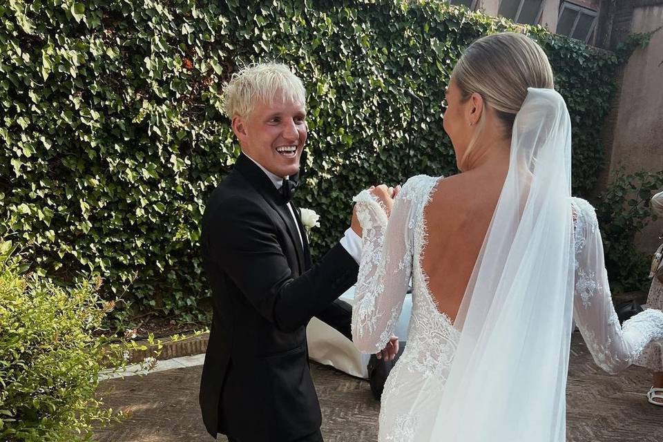Jamie laing n a black wedding tux looking at his new wife Sophie habboo who is facing him wearing a low bacl long sleeve lace wedding dress and veil