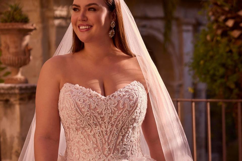 Plus size bride wearing a strapless corset ballgown dress with tulle floral applique on the skirt. She's also wearing a veil.