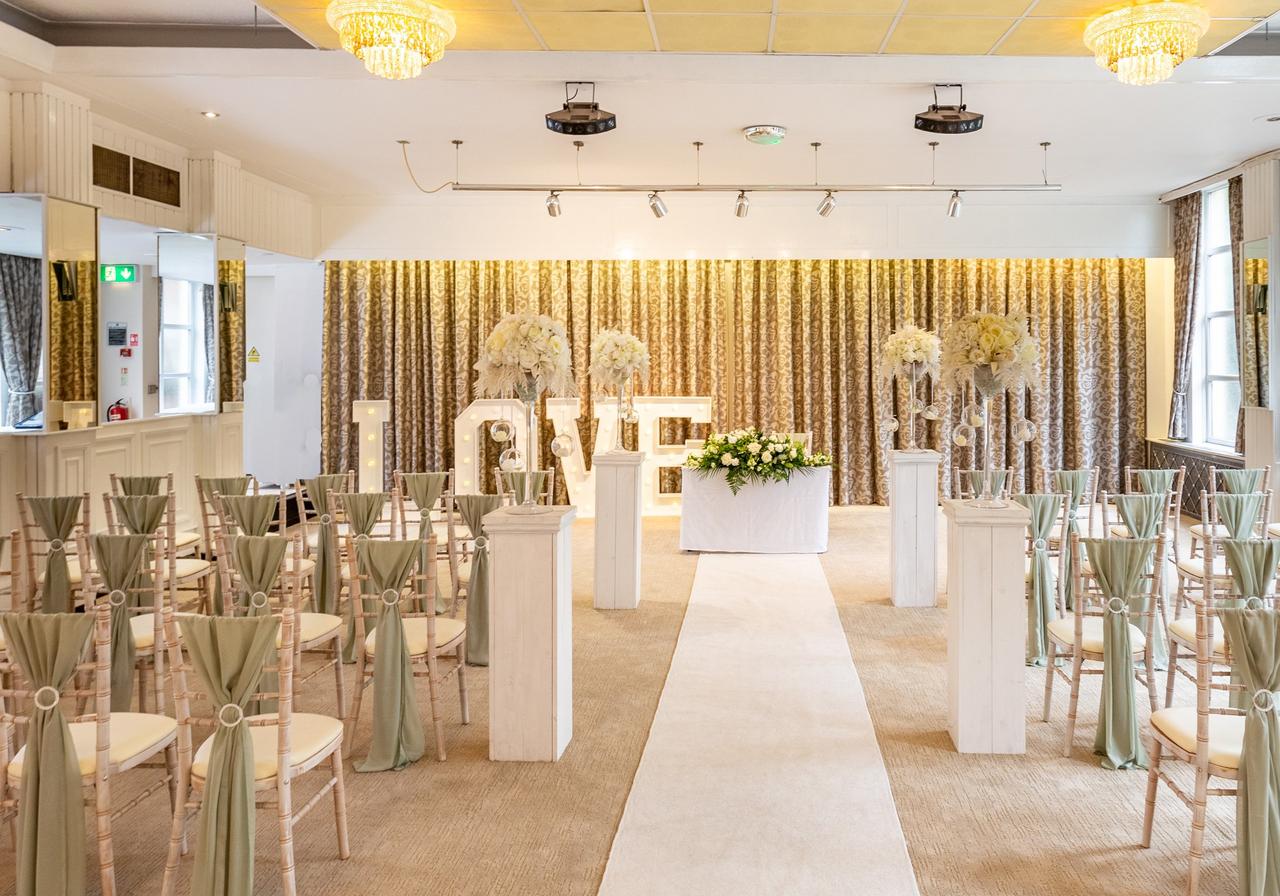 Interior of a country house hotel wedding venue set up for a ceremony with curtain backdrop and freestanding 'LOVE' lights.