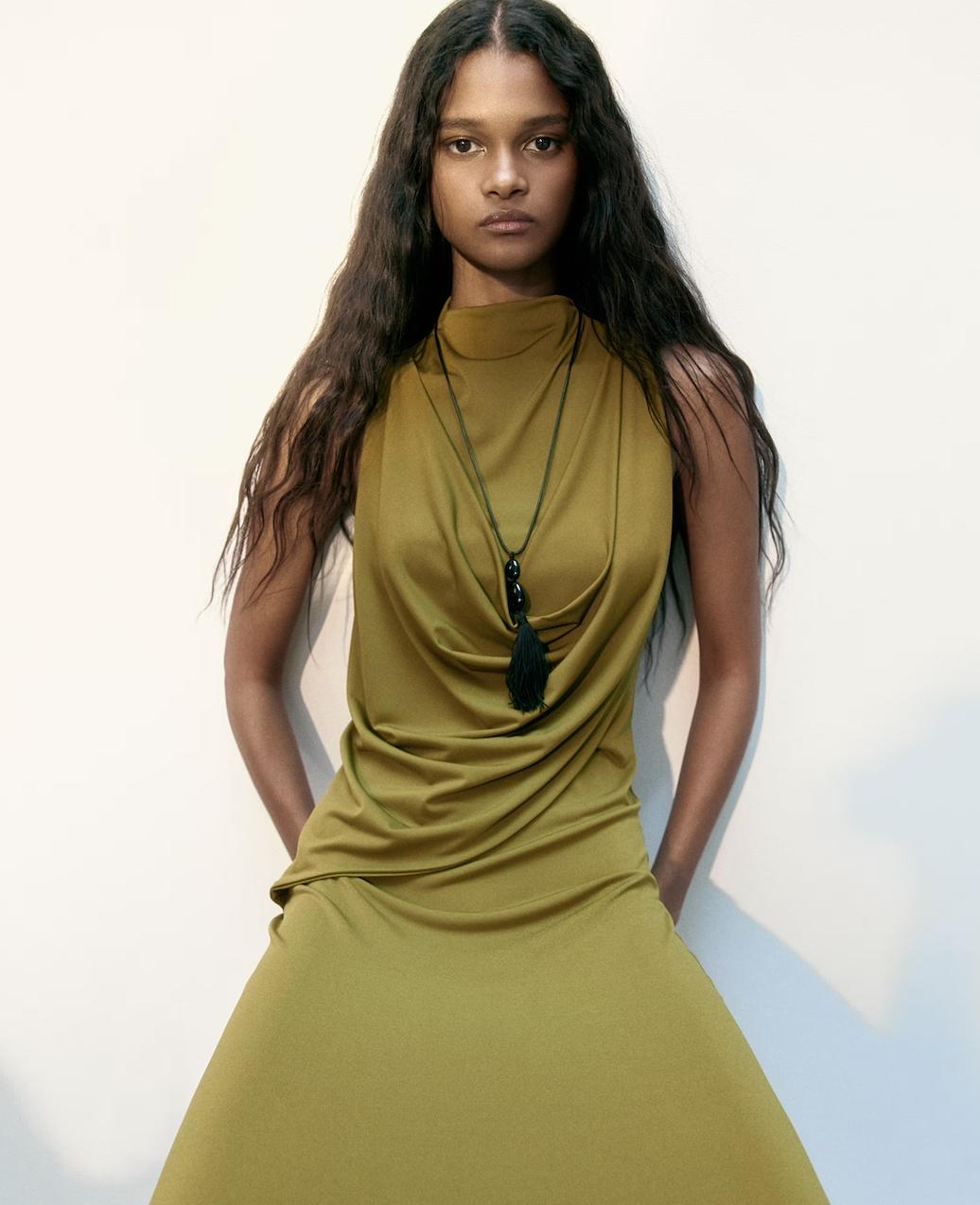 model wearing a khaki long draped dress with a pendant necklace