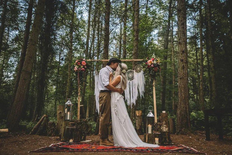 Bride and groom kiss in front of a boho display in a forest