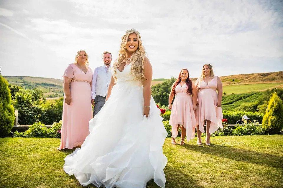 A bride in the foreground with three bridesmaids and a bridesman in pink themed clothing standing at different points in the background