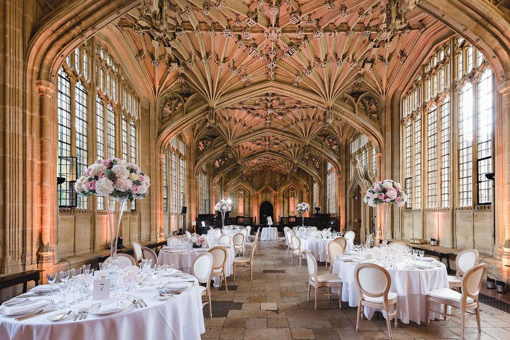 the interior of the bodleian libraries in Oxford, the grand stone dining hall with sculpted ceilings above round white tables dressed for a wedding