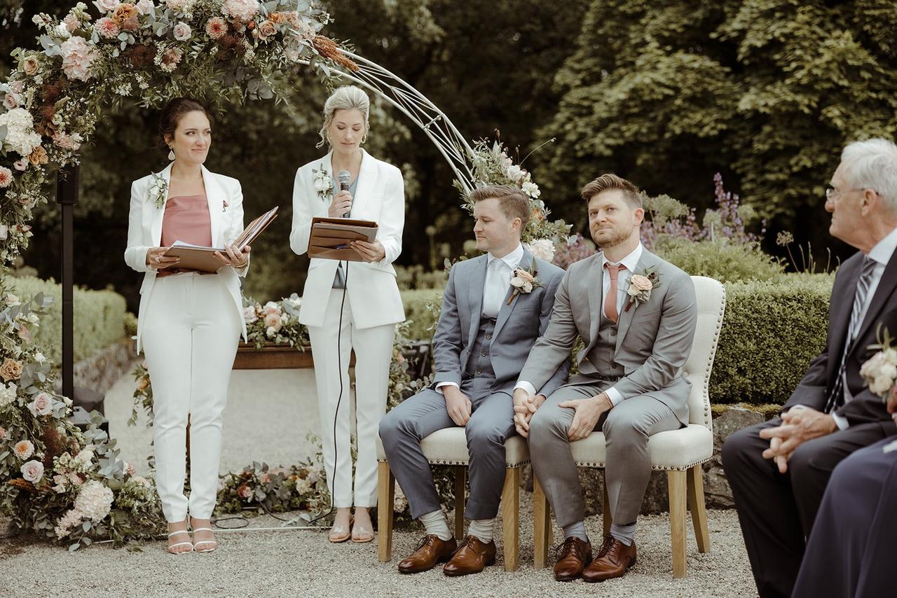 The officiants read into microphones as the grooms sit holding hands