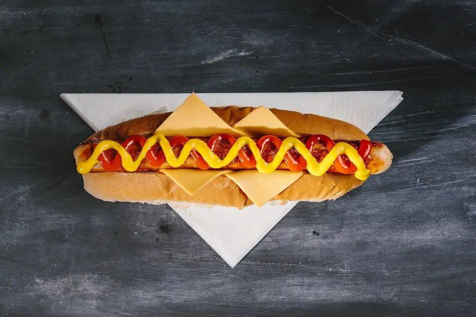 Hot dog on a napkin with cheese, ketchup and mustard