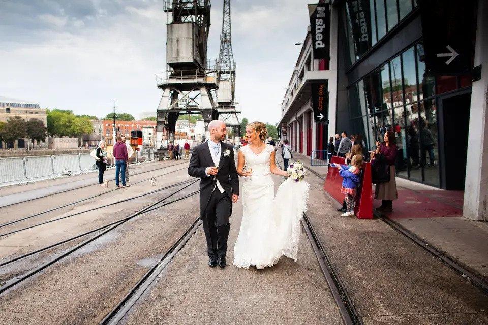 bride and groom walk by a river past an industrial wedding venue