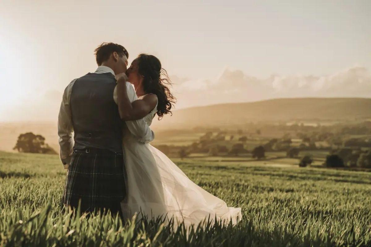 a wedding couple kissing at sunset in a field with hills and countryside in the background
