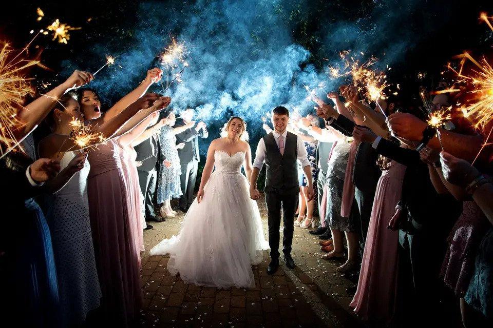 bride and groom walking hand-in-hand through a group of wedding guests with sparklers outdoors in the dark