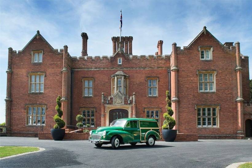Red brick country manor with manicured sculpted plants and a green vintage car parked outside