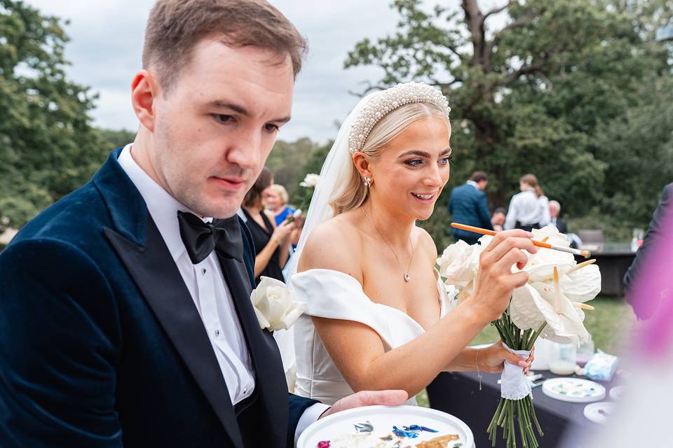 A bride and groom painting on a canvas at their wedding outside in a garden