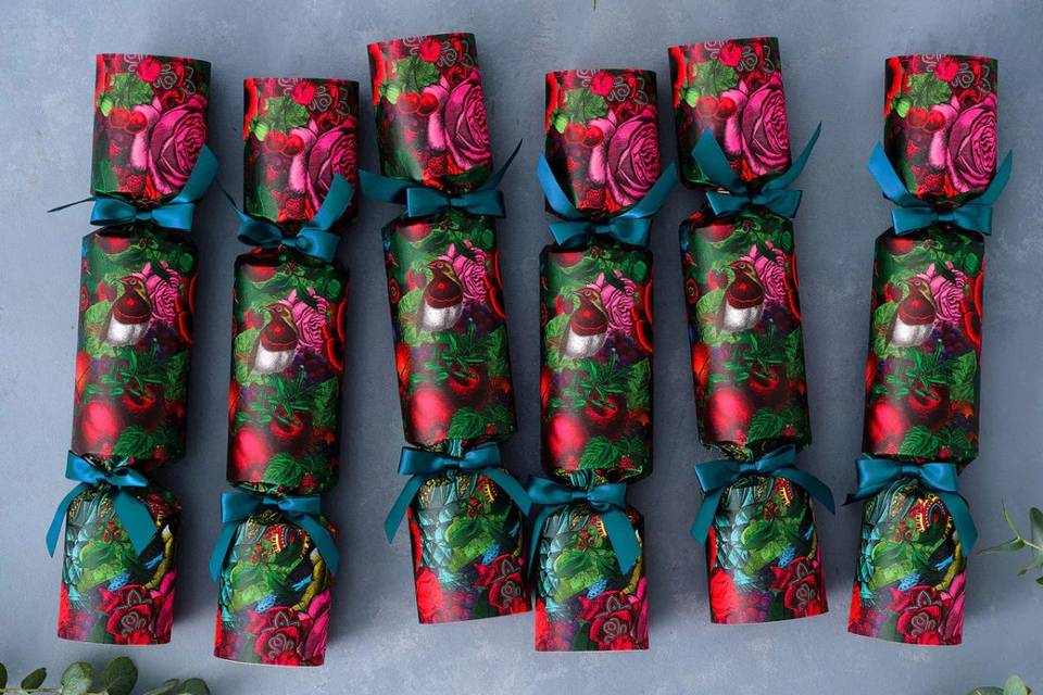 A row of six luxury christmas crackers each boasting a dark pink and green design with a robin on the front, and each tied with blue ribbon