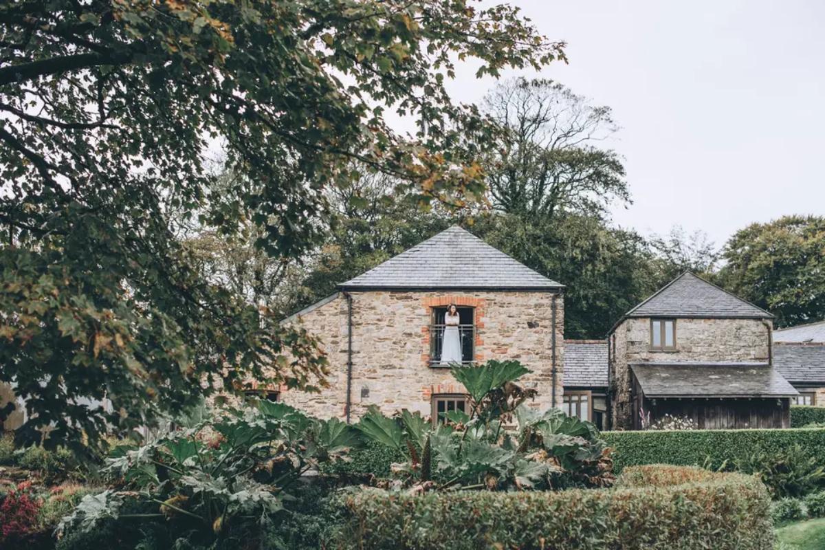 8 a far away shot of a bride standing on the thrashing balcony which overlooks the gardens oftrevanna wedding venue