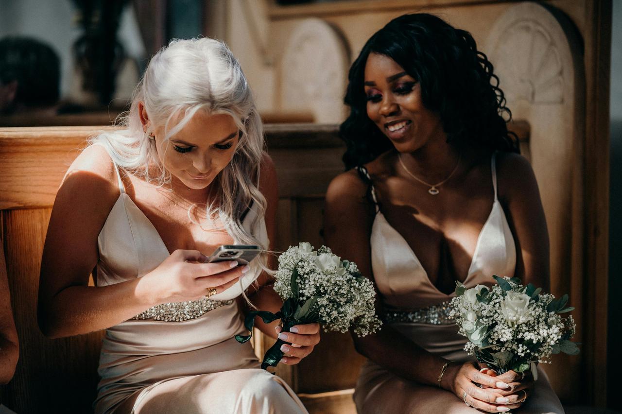 two bridesmaids looking at a phone during a wedding ceremony