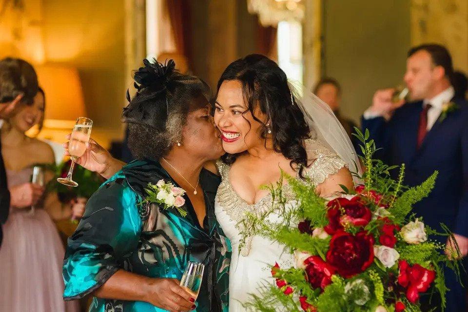 Bride being kissed by her mum on the cheek as she celebrates - her makeup is quite natural save for a bold, glossy red lip