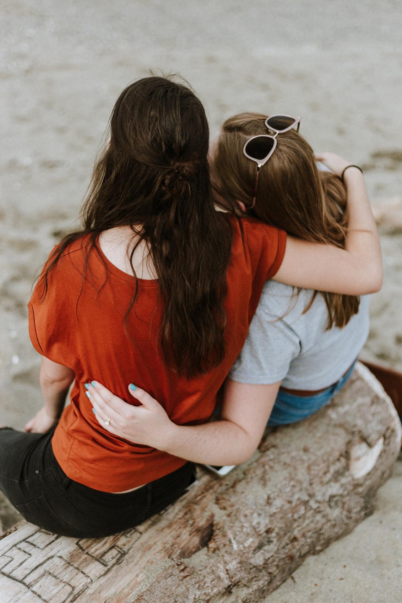 Female couple from behind with their arms around each other in a supportive post