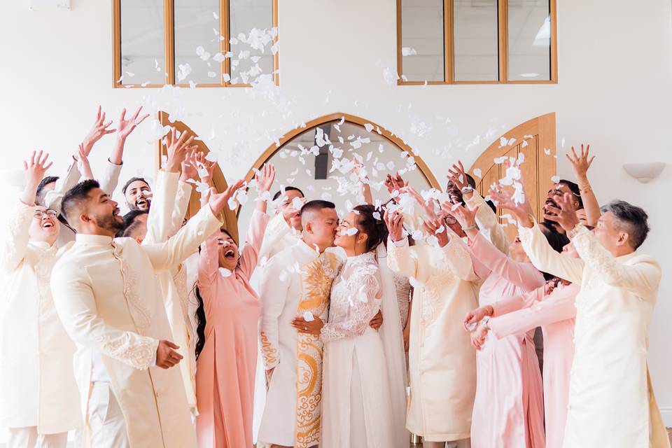 The wedding guests throw confetti over the bride and groom as they kiss