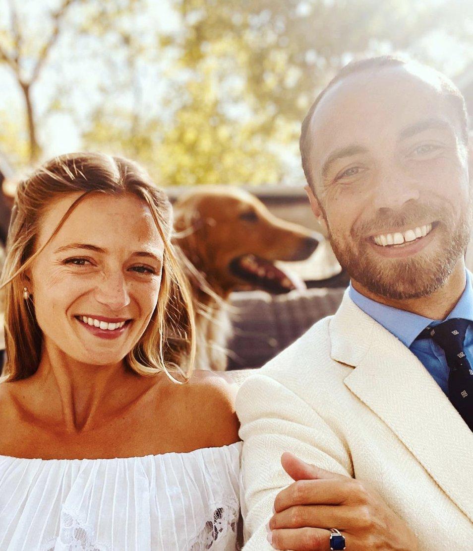 James Middleton in a cream suit, navy tie and light blue shirt linking arms with his new wife Alizee Thevenet who wears an off the shoulder Bardot white dress, pearl drop earrings and her dark blonde hair in a half up style