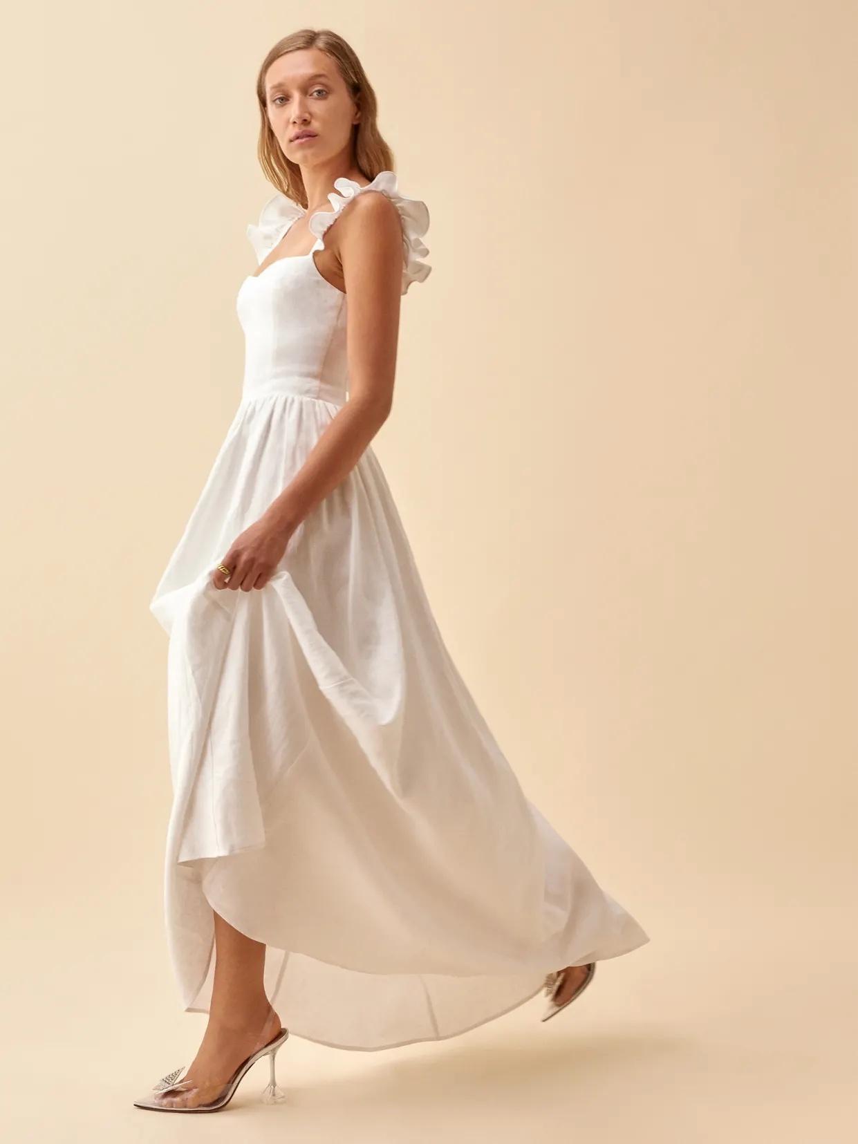 White woman with long blonde hair wearing a frill sleeved smocked white wedding dress with a flowing skirt and heels