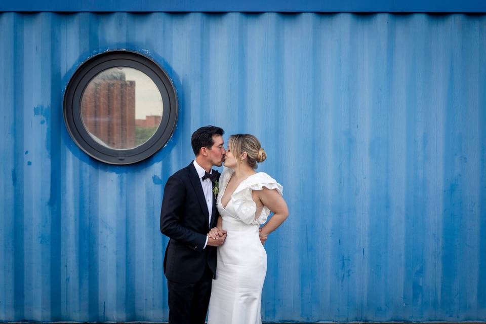 A bride and groom kissing in front of a blue wall