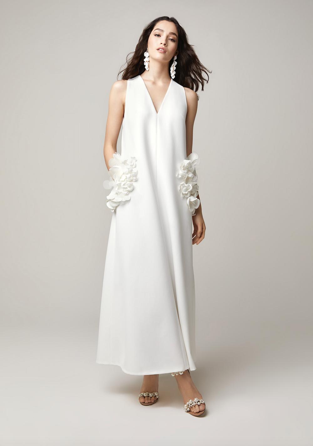 Asian woman with long brown hair wearing a sleeveless A line white tunic wedding dress with floral appliqué pockets and matching white drop earrings
