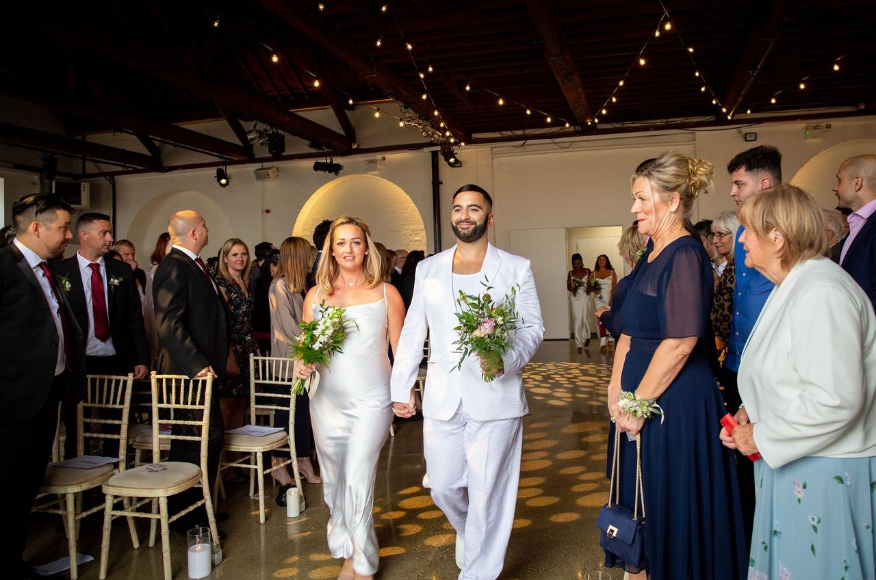 A bridesmaid and bridesman walk down the aisle wearing ivory