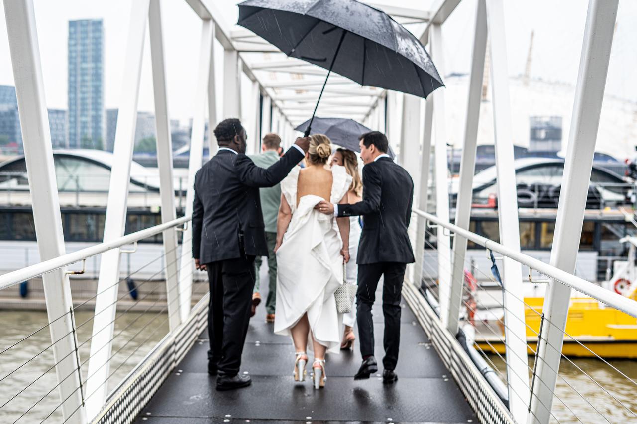A groomsmen holds an umbrella over the bride as the groom holds up her train