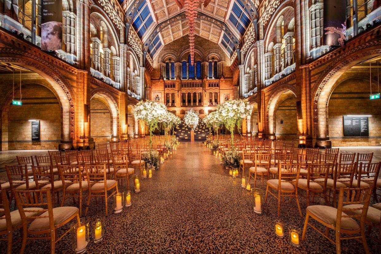A gold-lit hall in the museum set up with Chiavari chairs, candles, and white florals for a ceremony
