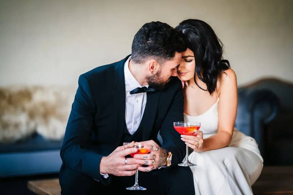 Couple sharing a romantic moment together whilst eloping. They wear wedding attire and each have a cocktail