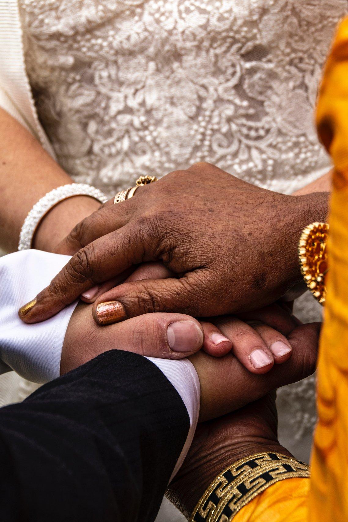 Wedding guest in yellow robes and gold jewellery joining hands with a bride in an embellished ivory dress and groom in a white shirt