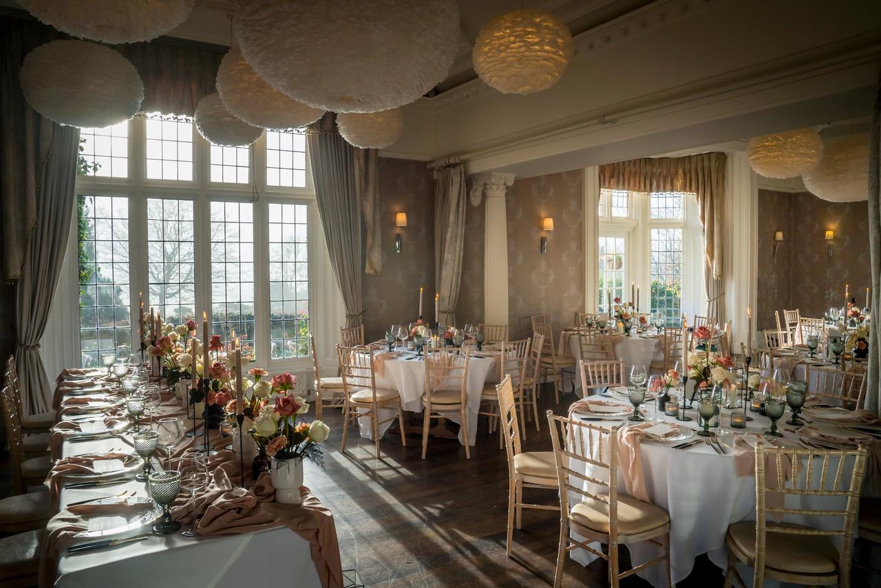 Interior of a manor house wedding venue set up for a wedding reception with round tables and chiavari chairs.