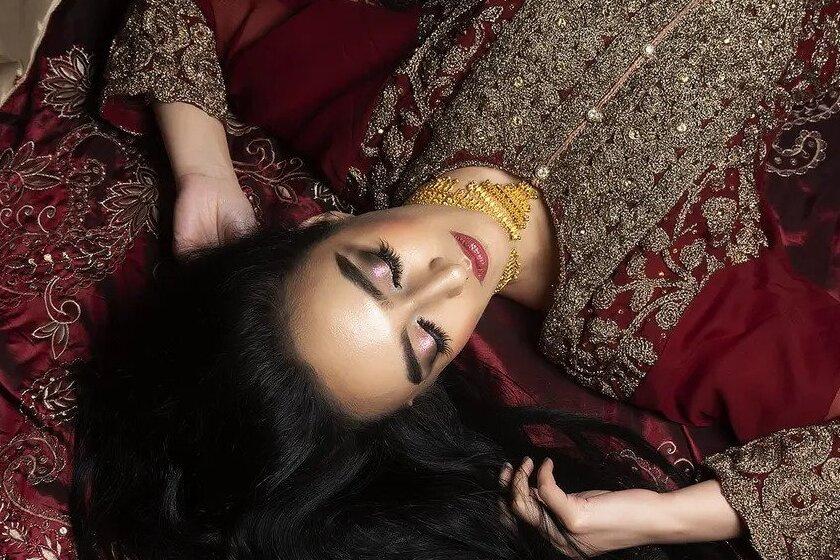 A bride dressed in traditional Indian wedding dress lying down with her eyes closed to display her eye makeup