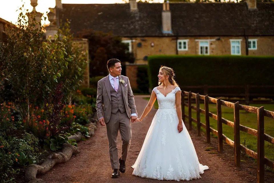 Bride and groom walk hand in hand down a country lane away from a wedding venue 
