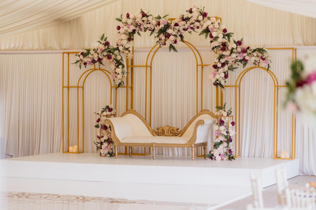 Three metal arches behind lounge chair on stage with purple and white flowers